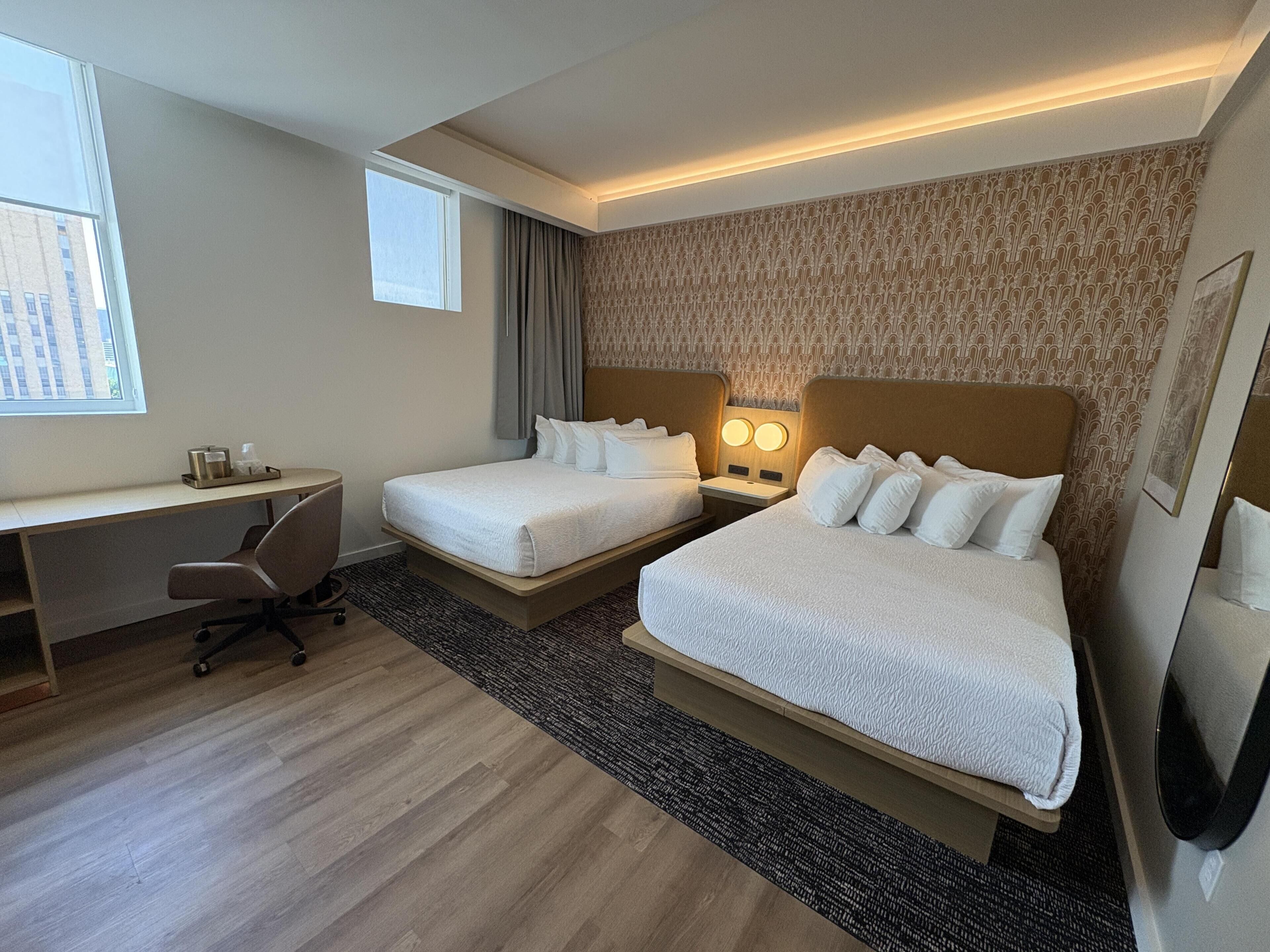 A hotel room with two beds, a desk, and a chair.