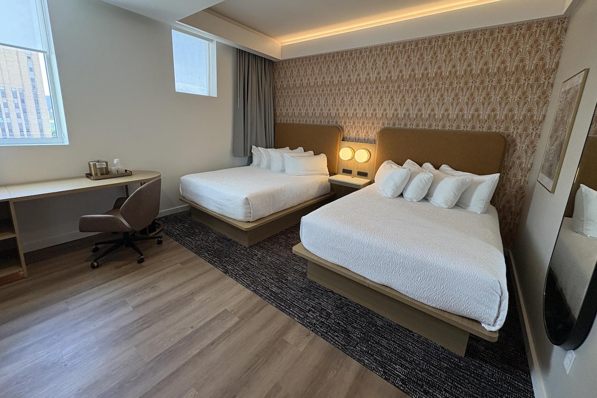 A hotel room with two beds, a desk, and a chair.