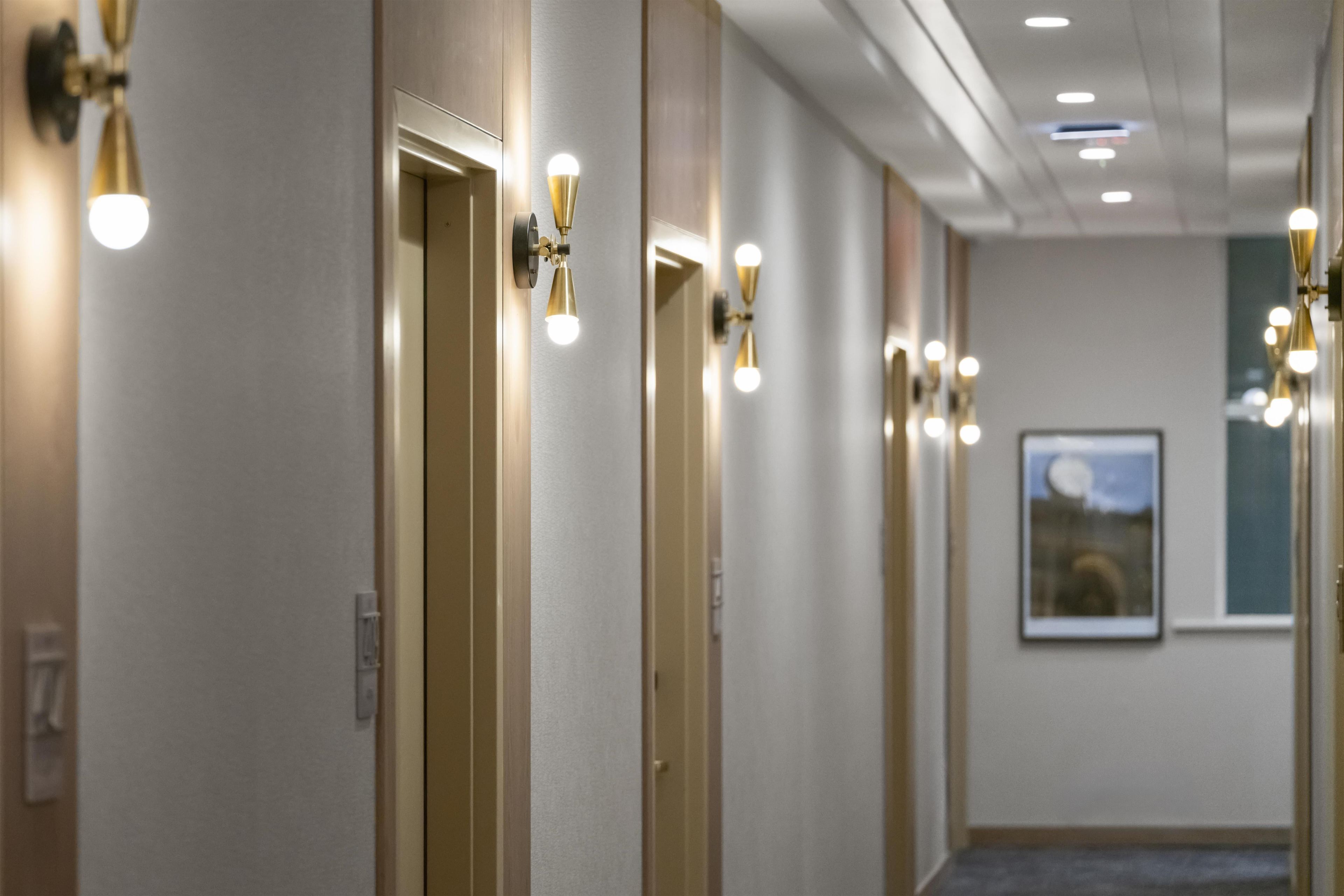 A hotel hallway with doors, wall-mounted lights, and a framed picture on the wall.