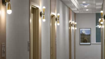 A hotel hallway with doors, wall-mounted lights, and a framed picture on the wall.