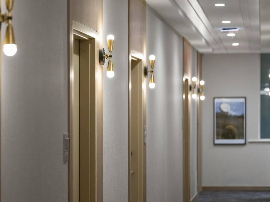 A hotel hallway with doors, wall-mounted lights, and a framed picture on the wall.