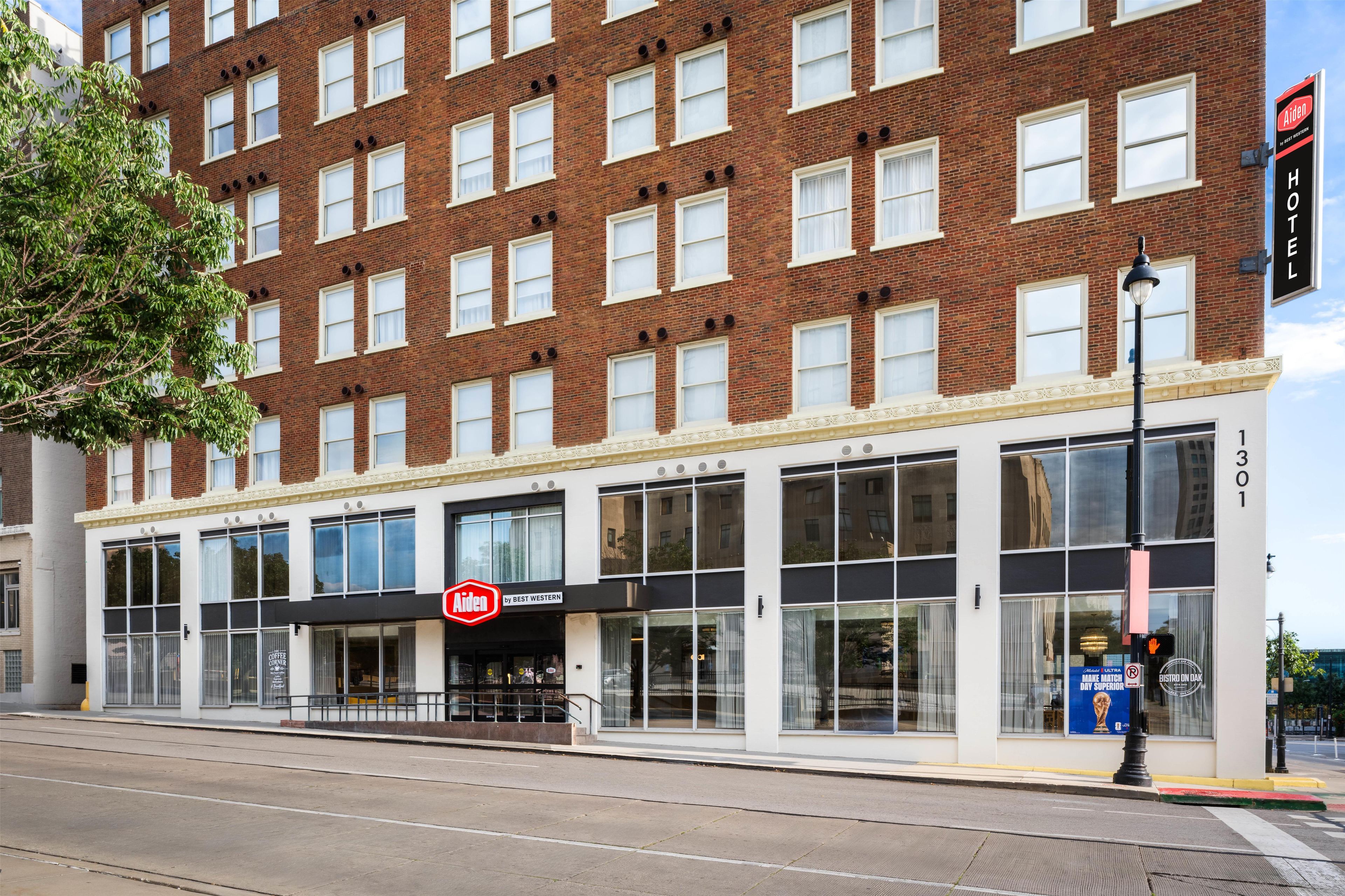 A hotel with a red and white sign, large windows, and a street view.