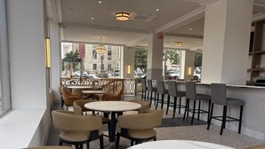 A café with round tables and chairs, large windows, and a view of the street.