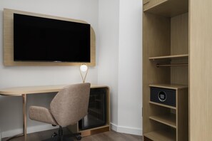 A modern office space with a mounted TV, a desk, a chair, and a built-in safe. - Aiden By Best Western Kansas City Downtown (Kansas City)
