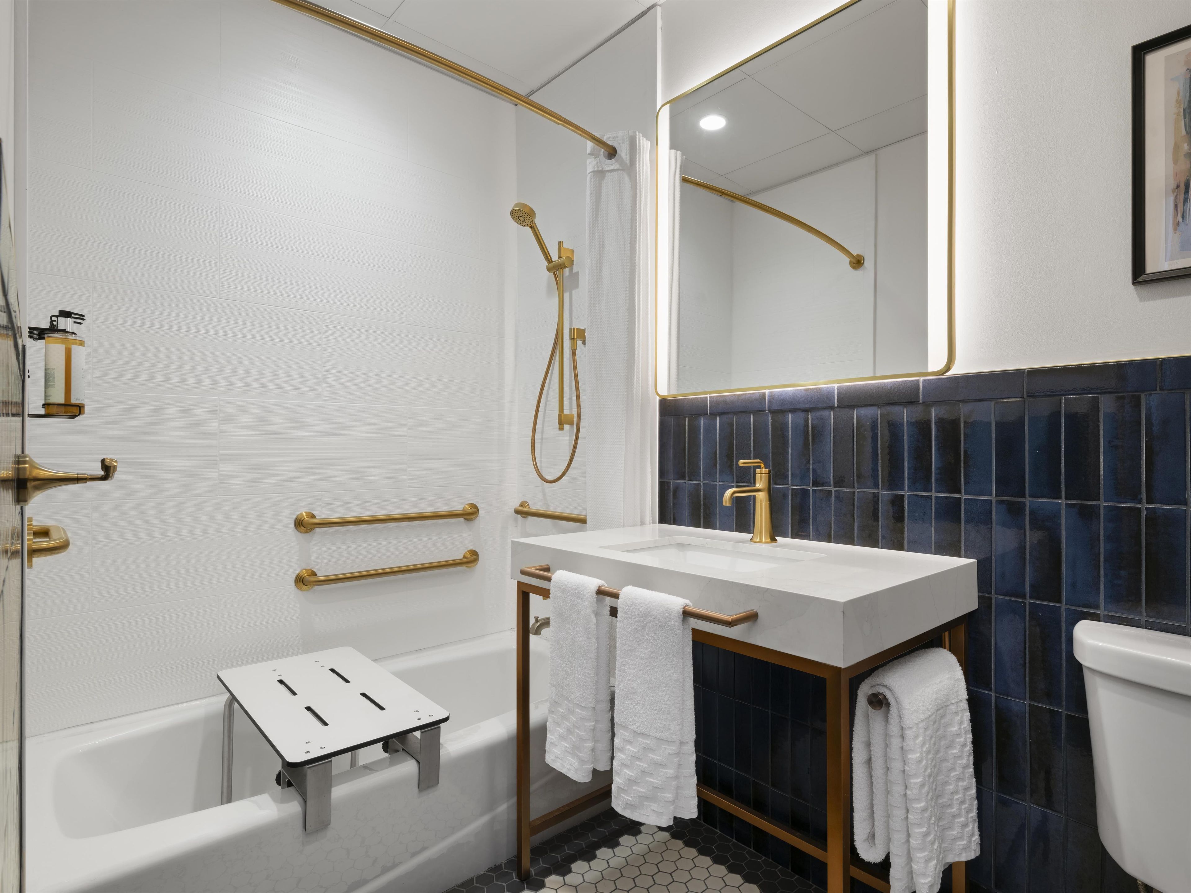 Un baño moderno con una bañera blanca, un tocador con grifo dorado y una pared revestida de azulejos azul oscuro.