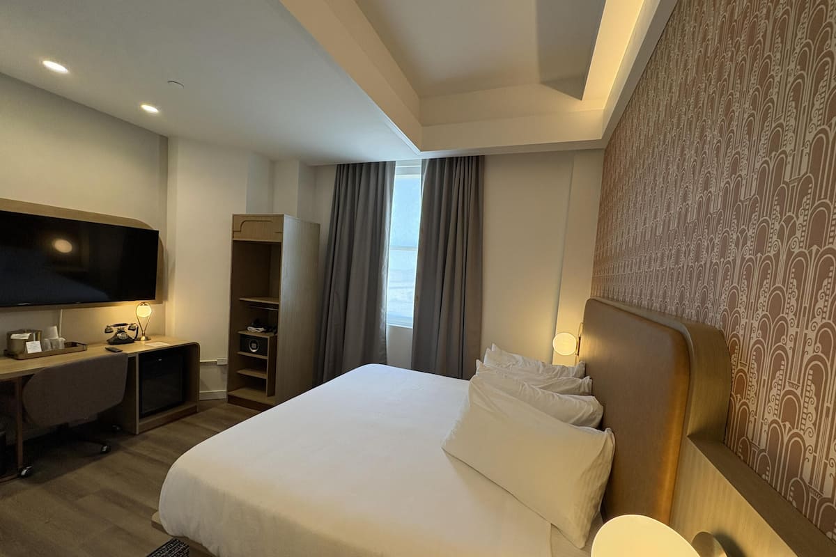A hotel room with a bed, a desk with a TV, a wardrobe, and a window with curtains.