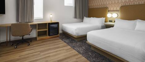 A hotel room with two beds, a desk, a chair, a TV, and a patterned wall.