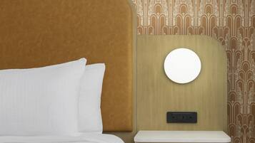 A bed with white bedding, a round mirror on a wooden nightstand, and a wall with a patterned wallpaper.