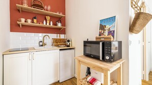 Una cocina compacta con armarios blancos, encimera de madera, un lavabo, microondas y una pequeña mesa con una cesta y una toalla.