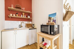 A compact kitchen with white cabinets, a wooden countertop, a sink, a microwave, and a small table with a basket and a towel. - Hotel-Style Suite Studio 50m from Croisette (Cannes)