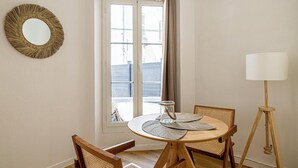 Una habitación con una mesa redonda de madera, dos sillas, una lámpara de pie, un espejo y un ventanal con vistas a edificios.