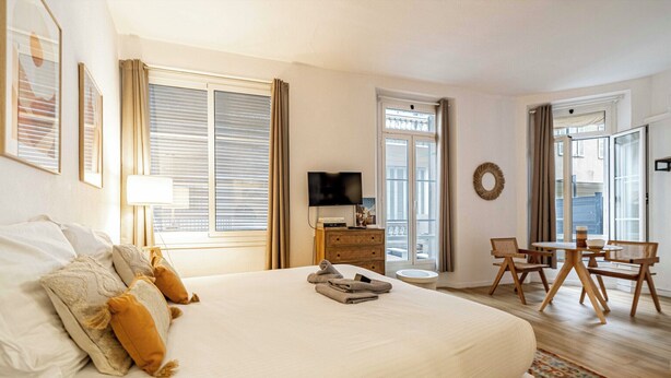 Habitación de hotel con una cama grande, un escritorio con sillas, un televisor y una ventana con cortinas.