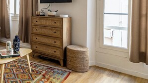 Una habitación con un aparador de madera, un televisor montado en la pared, un taburete redondo pequeño y una alfombra colorida.
