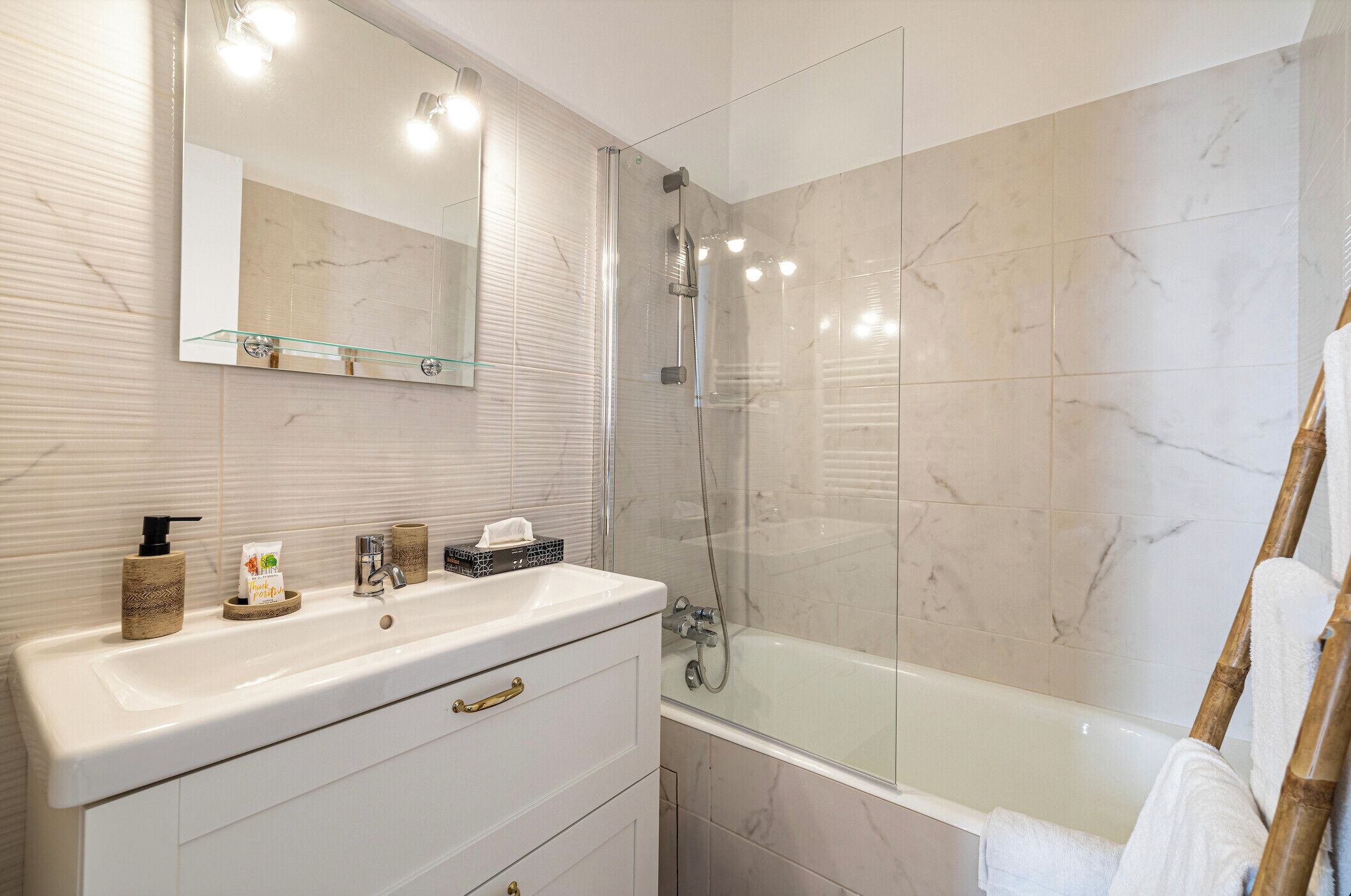 Un baño moderno con ducha de vidrio, tocador blanco con espejo y bañera.