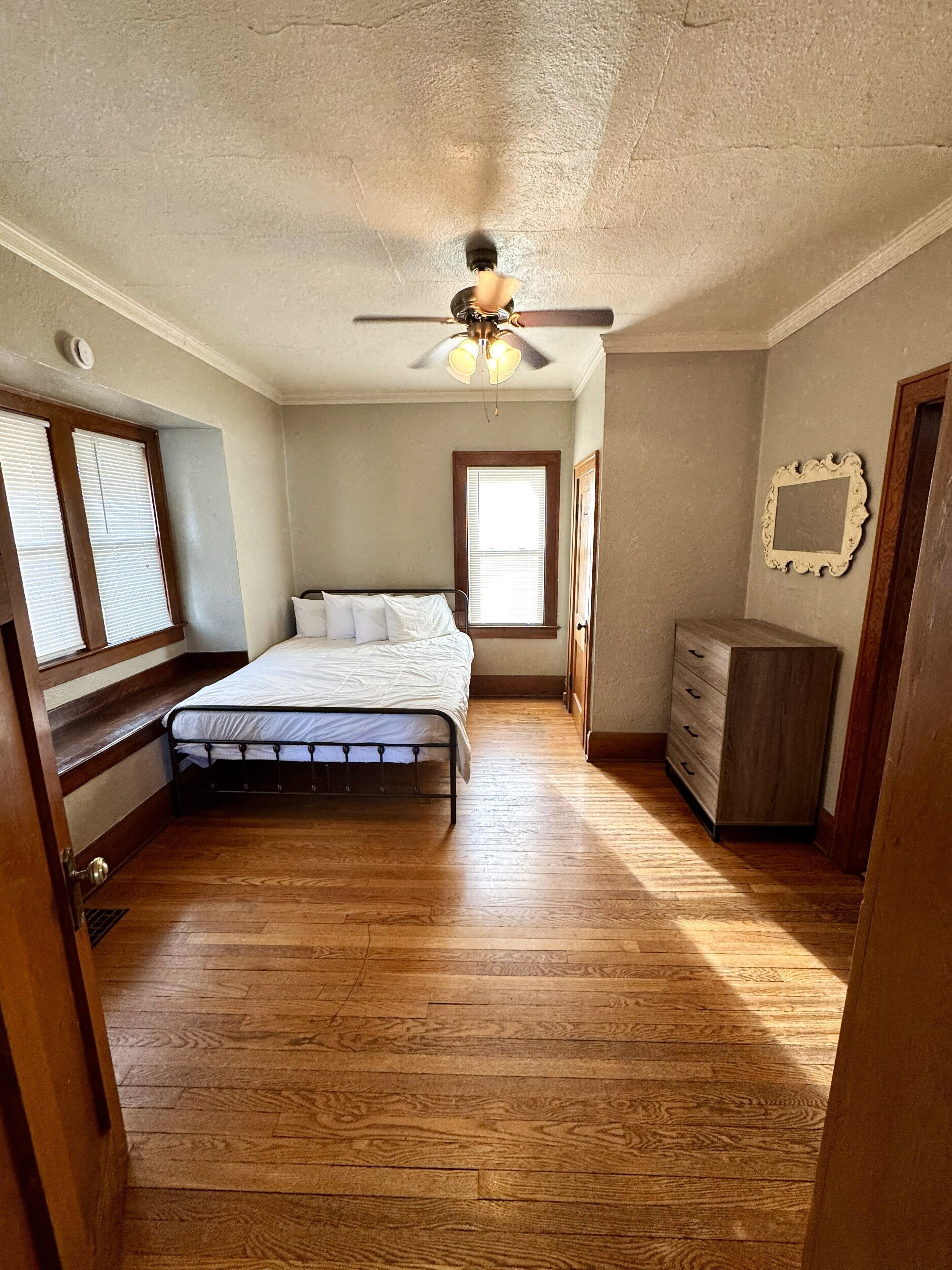 Un dormitorio con cama, piso de madera, ventilador de techo y cómoda.