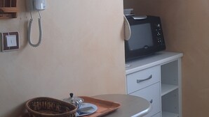 A kitchenette with a microwave, kettle, and a small shelf with cups. There is a phone on the wall and a basket on a cart. - "Le Pesquit" large, fully-equipped 36m2 studio on one level: private terrace. (Lescar)