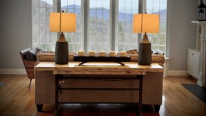 Ein Holztisch mit zwei Lampen, einem Kerzenständer und Blick auf Berge durch große Fenster.