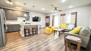 A modern kitchen with a central island, a dining area with yellow chairs, and a living room with a sofa and a coffee table. - 4 Bedroom / 4.5 Bathroom, Unit B_ Newly Built - Med Center / NRG / Downtown / UH (Houston)