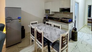 Una cucina compatta con mobili bianchi, piano cottura integrato e zona pranzo con tavolo e sedie in marmo.