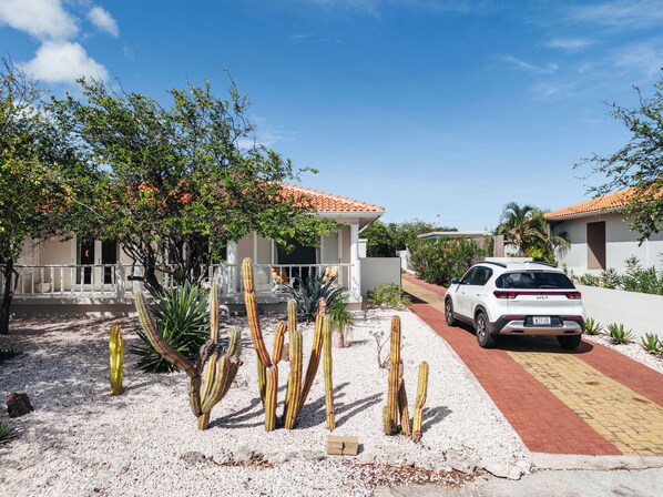 A residential area with houses, a white car parked in front, and cacti in the foreground. - Modern 3 bedroom villa with private pool at gated Coral Estate Beach Resort (Sint Willibrordus)