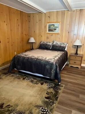 Ein Schlafzimmer mit Holzvertäfelung, einem Bett mit floralem Überwurf, zwei Nachttischlampen und einem kleinen Holz-Nachttisch.