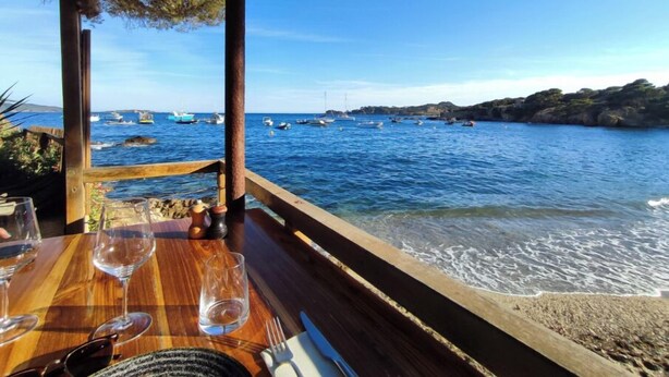 A wooden table with glasses and cutlery, overlooking a coastal area with boats and rocky terrain. - Le Clos Ferté villa in Le Lavandou (Le Lavandou)