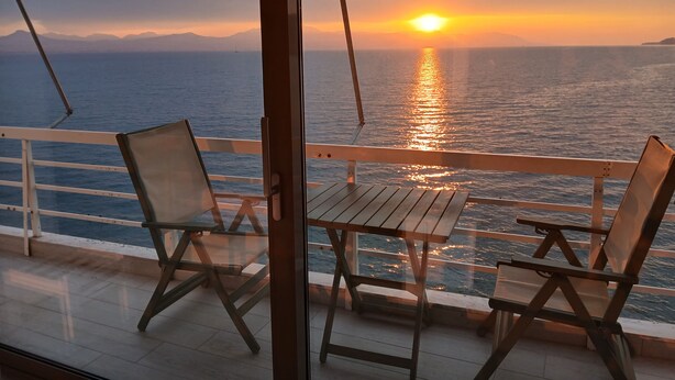 Un balcon avec deux chaises en bois et une table, d’où l’on peut admirer le coucher de soleil sur l’océan.