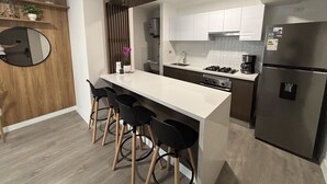 Uma cozinha moderna com uma ilha central, banquetas, forno embutido e uma geladeira.