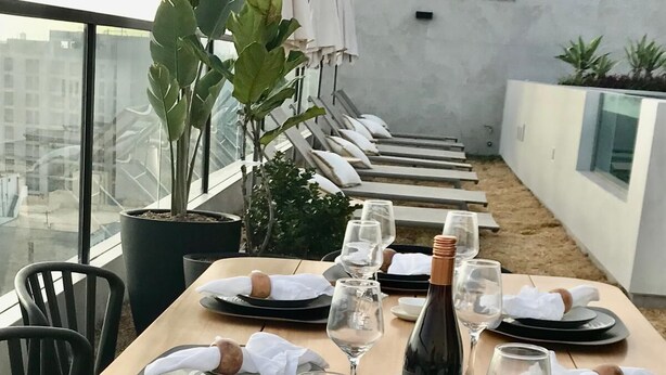 Uma área de refeições no terraço com várias mesas preparadas para uma refeição, cada uma com pratos, talheres e copos de vinho.
