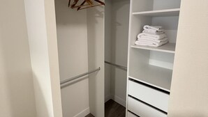 Um closet espaçoso com prateleiras e gavetas brancas, uma barra para pendurar roupas e toalhas dobradas com cuidado.