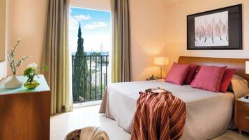 Habitación de hotel con una cama grande, una mesita de noche, una lámpara, vistas al exterior y una obra de arte enmarcada en la pared.