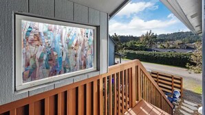 Una escalera de madera lleva a un balcón con un ventanal de vitral y vistas a un barrio residencial.