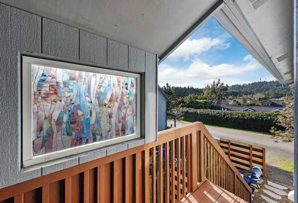 A wooden staircase leading to a balcony with a stained glass window and a view of a residential area.