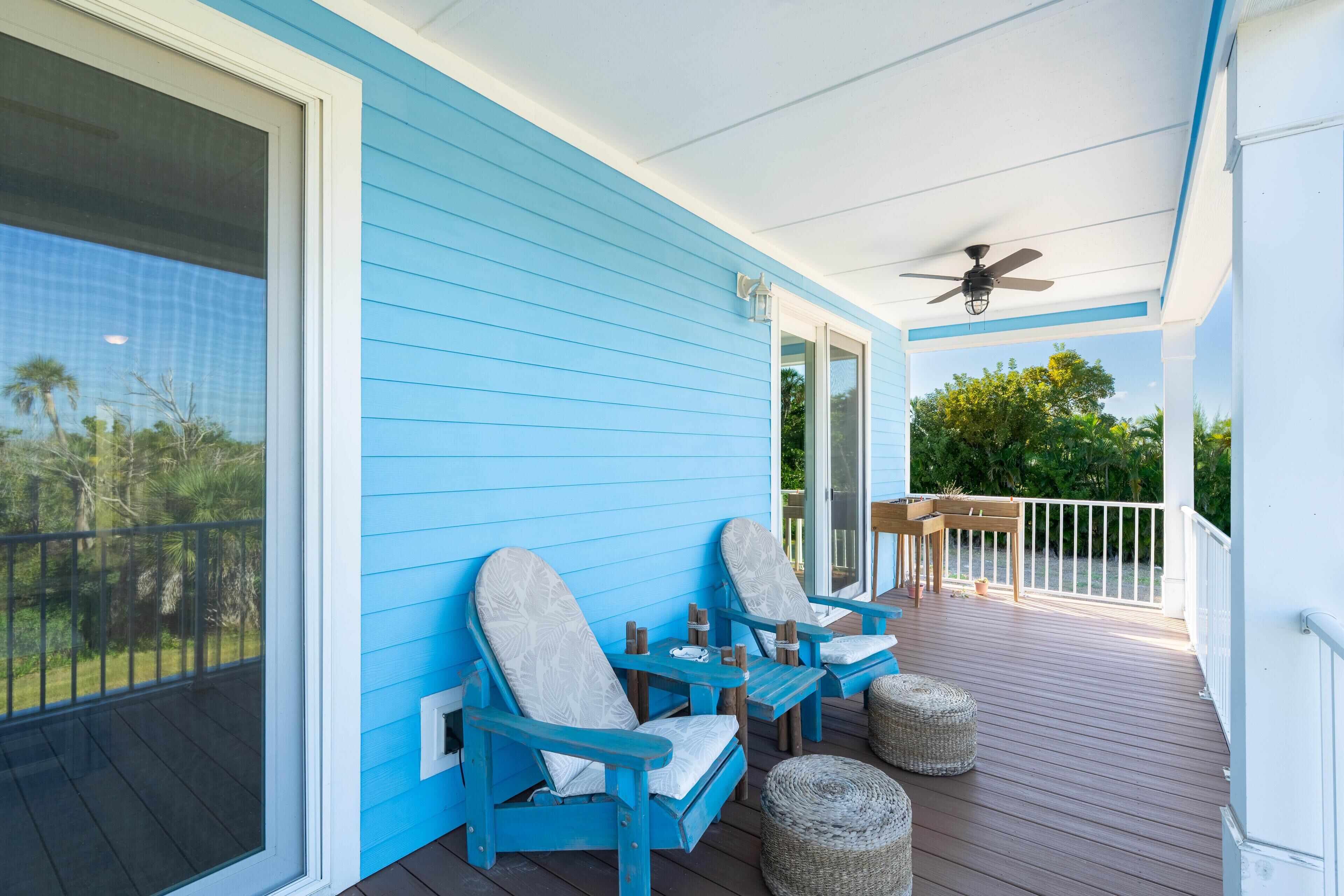 A covered porch with blue walls, two chairs, a table, and a ceiling fan.