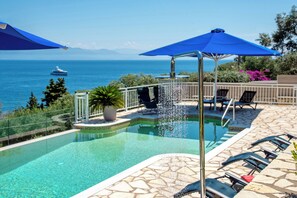A swimming pool with a fountain, lounge chairs, and a view of the sea. - Villa Avgerini Paxos III: Breathtaking sea views, private terrace & amazing pool (Gaios)