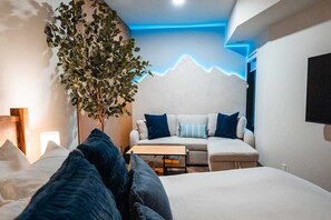 Una habitación de hotel moderna con una cama, un sofá, una mesita de centro y una planta grande.