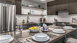 Une cuisine moderne dotée d’appareils électroménagers en acier inoxydable, d’un îlot central aménagé en coin repas et d’objets décoratifs disposés sur des étagères.