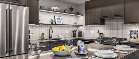 Una cocina moderna con electrodomésticos de acero inoxidable, una isla central con comedor y objetos decorativos en estantes.