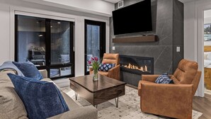 Un salon moderne avec une cheminée, un téléviseur à écran plat fixé au mur et un canapé agrémenté de coussins bleus.