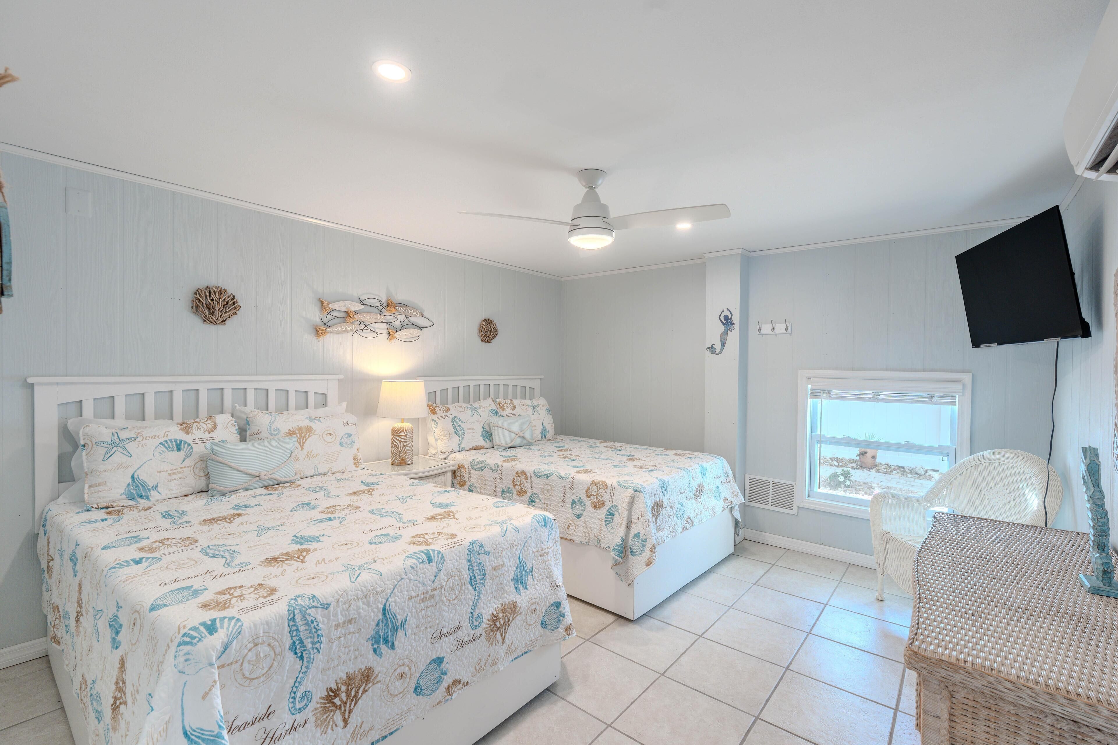 A bedroom with two beds, a ceiling fan, a TV, and a window with a view.