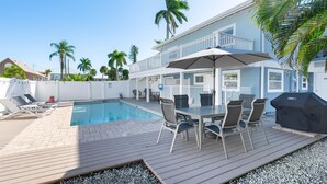 Uma área à beira da piscina com mesa e cadeiras, churrasqueira e piscina.