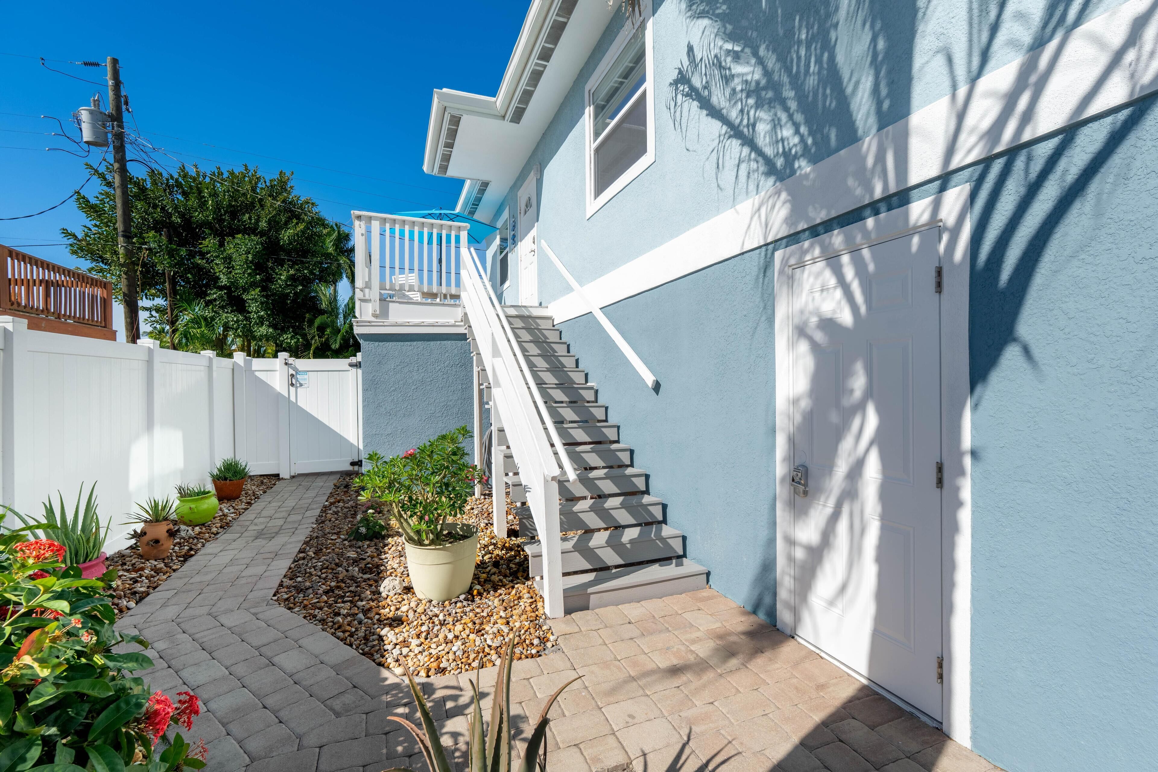 A residential property with a staircase leading to a garage, a white fence, and potted plants along a pathway.