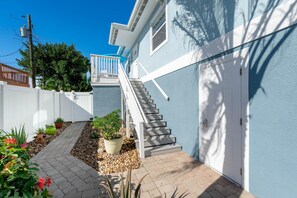 A residential property with a staircase leading to a garage, a white fence, and potted plants along a pathway. - Blue Pearl Manor Upper (Fort Myers Beach)
