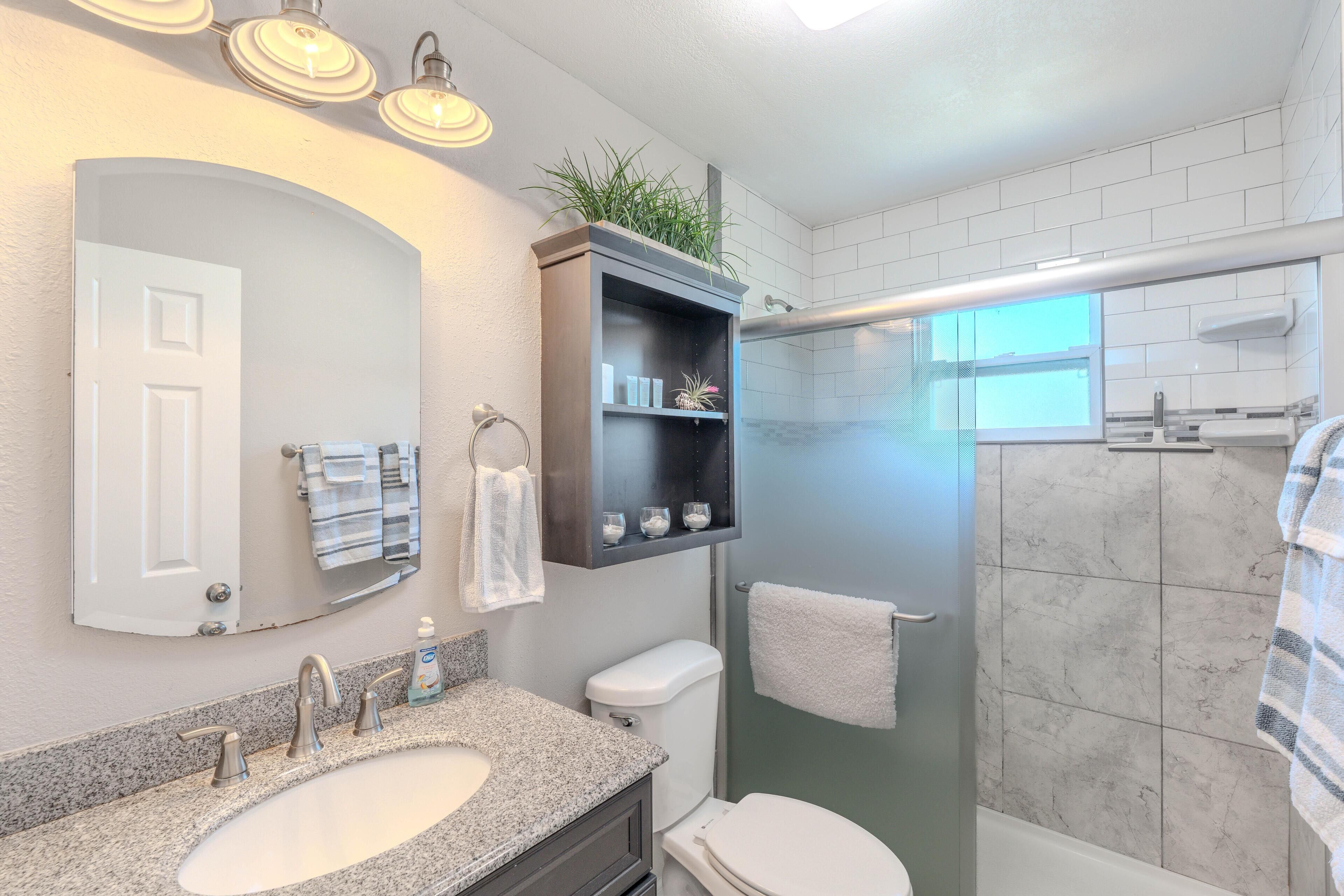 A bathroom with a double sink, a toilet, a shower enclosure, and a mirror with a shelf above.