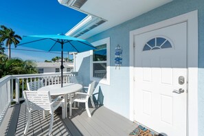 A white deck with a table and chairs, a blue umbrella, and a white door with a keypad lock. - Blue Pearl Manor Upper (Fort Myers Beach)