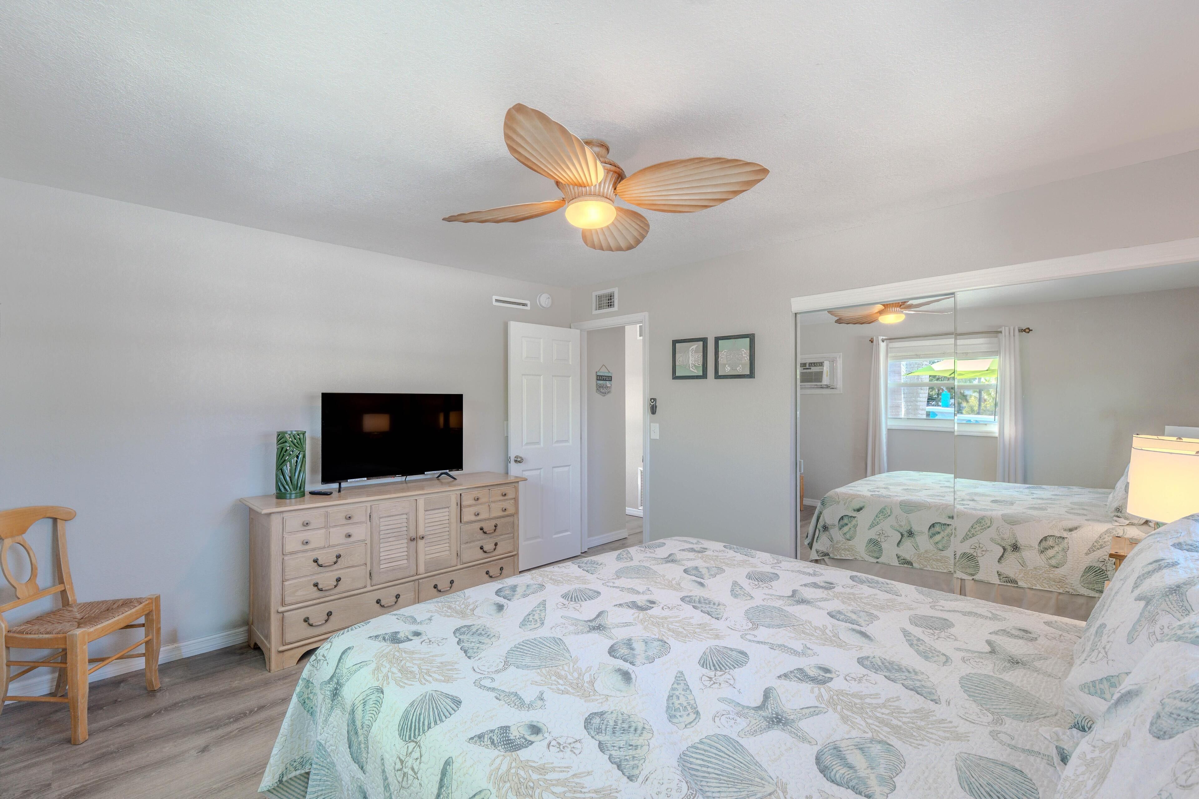 A bedroom with a bed, a dresser, a television, and a ceiling fan.