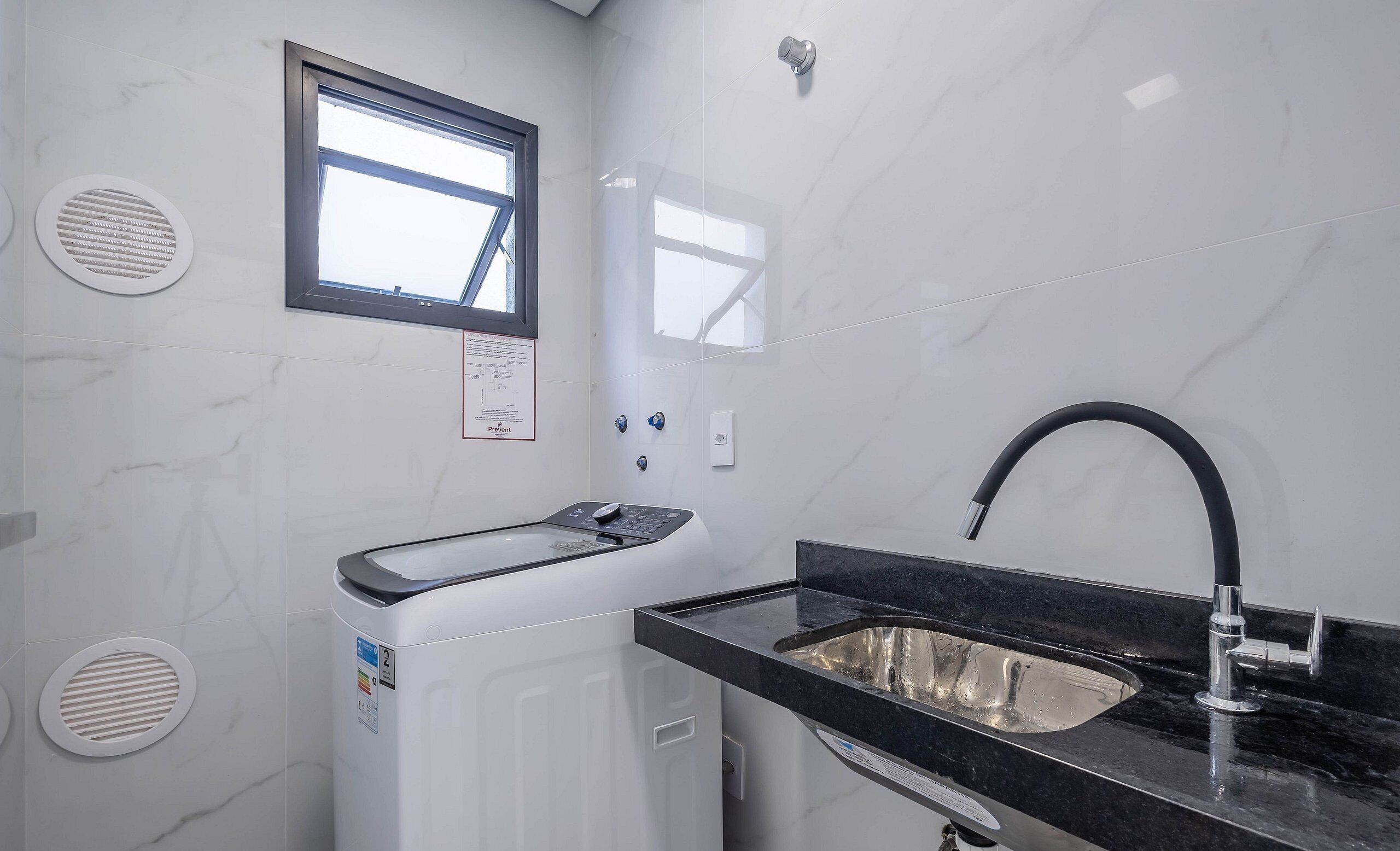 A modern bathroom with a built-in washing machine, a sink with a black countertop, and a window providing natural light.