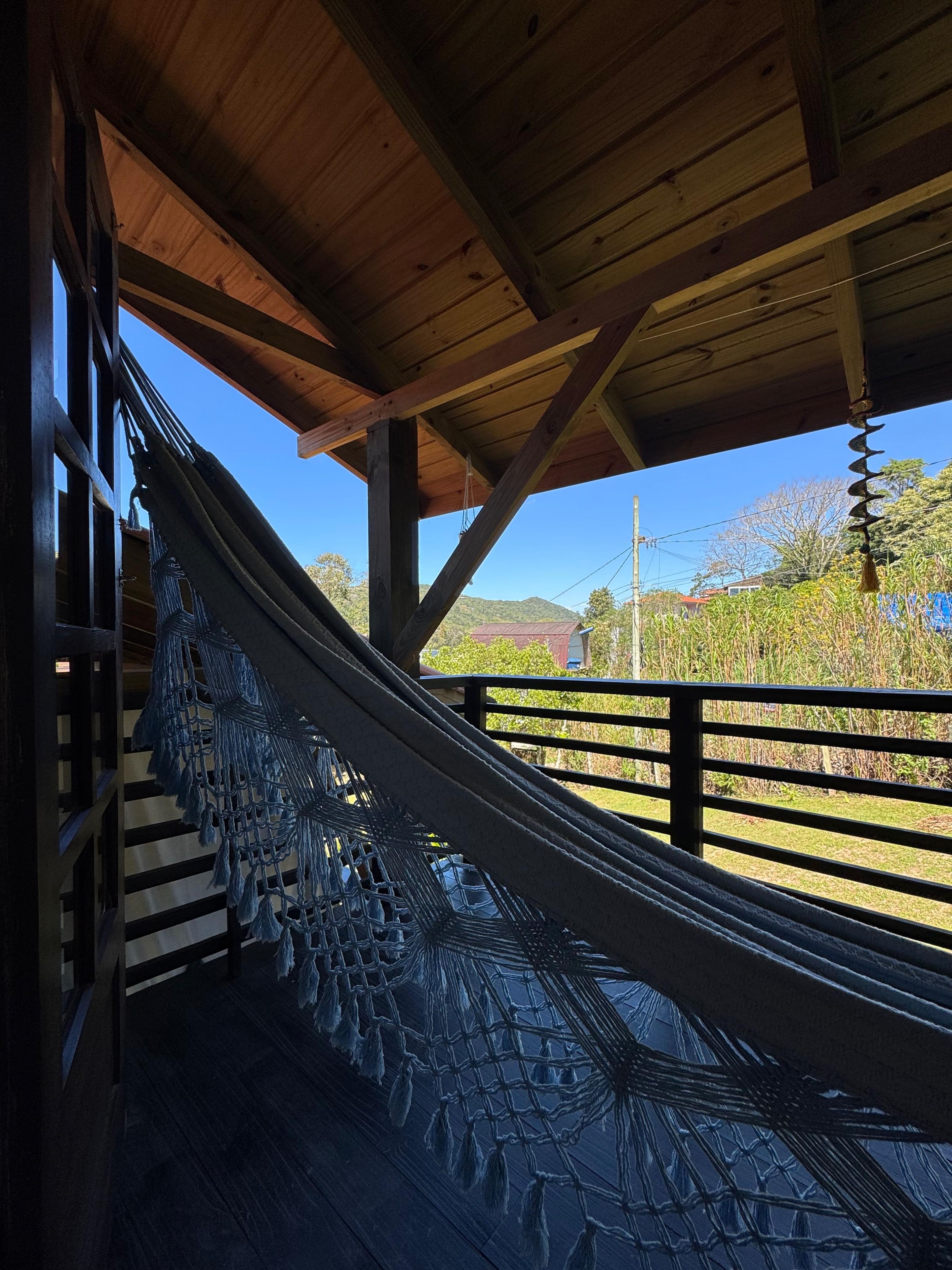 A hammock under a wooden structure with a view of a rural landscape.