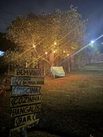 Escena nocturna al aire libre con letreros iluminados que señalan diferentes servicios, como piscina, bar y restaurante.