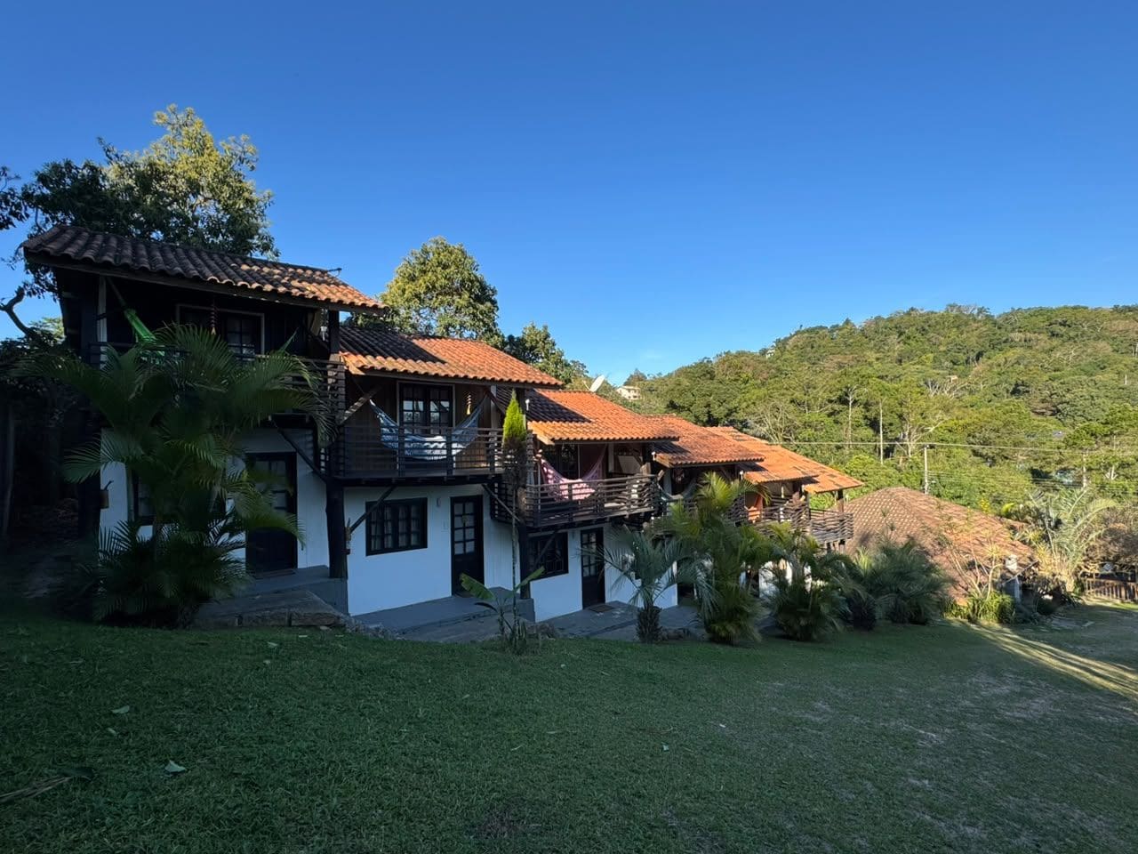 A two-story house with a red-tiled roof, surrounded by greenery and hills.